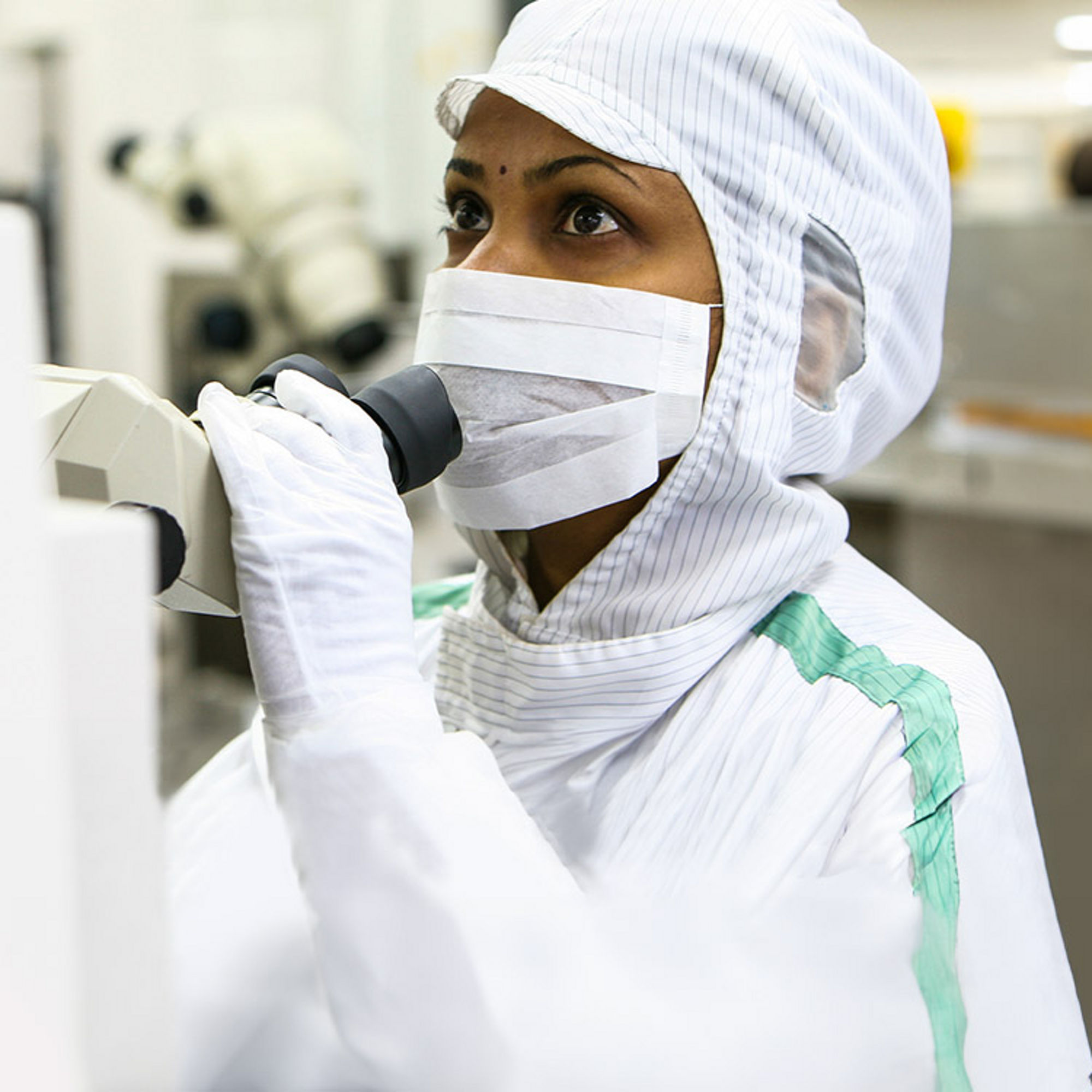 A woman in a cleanroom suit handling equipment in a laboratory setting