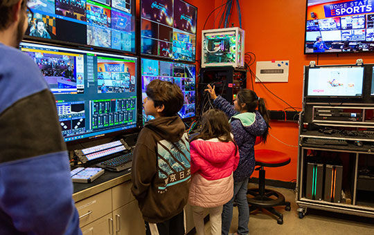 Group of children in front of a bank of monitors showing various STEM-related images.