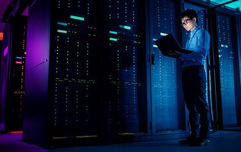 Man standing in dark data center holding a laptop