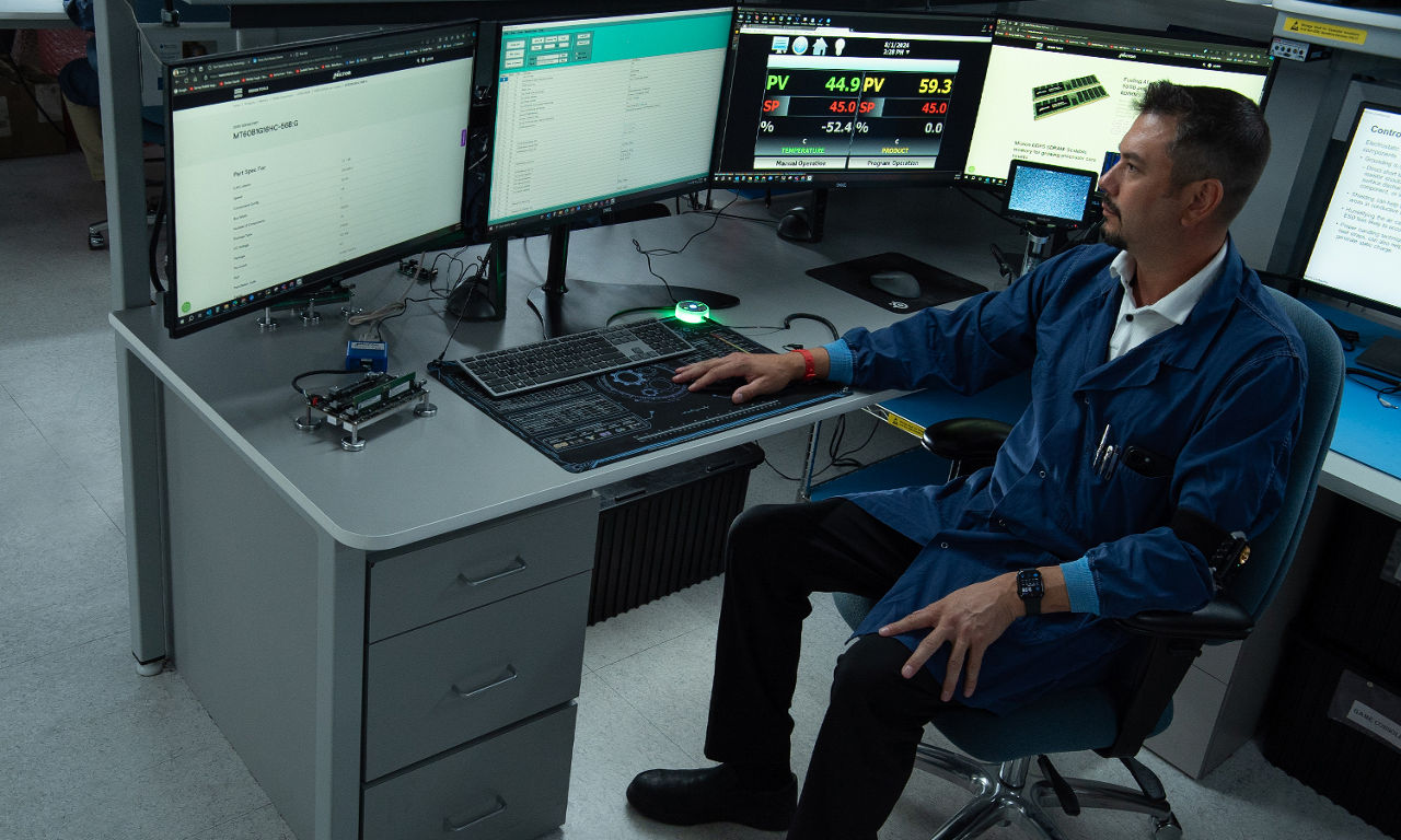 A person in a blue shirt and dark pants sitting at a workstation with multiple computer monitors