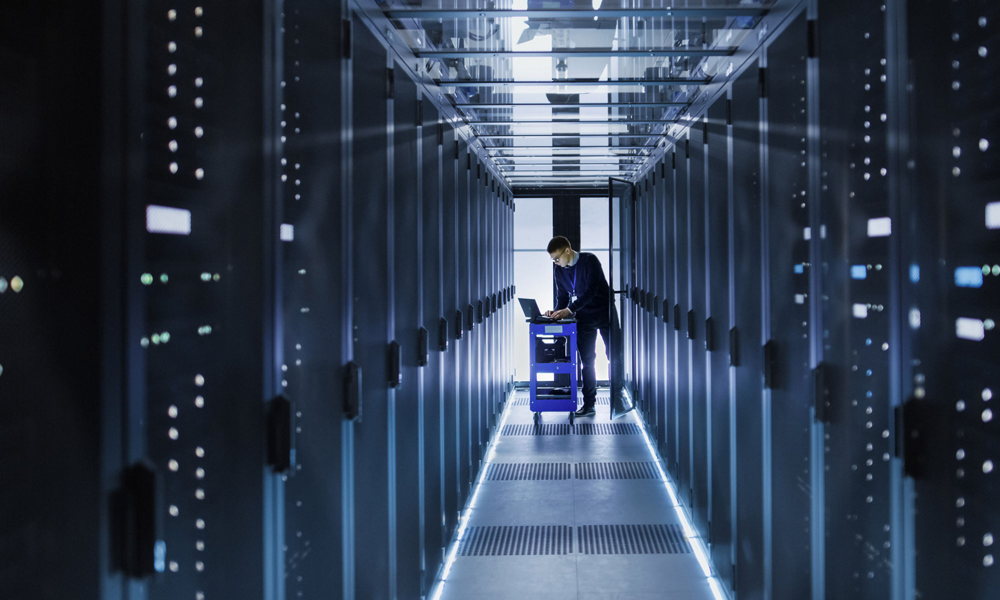 IT Engineer With Crash Cart Puts Hard Drives into Open Rack Server Cabinet. He's Working in Big Data Center.