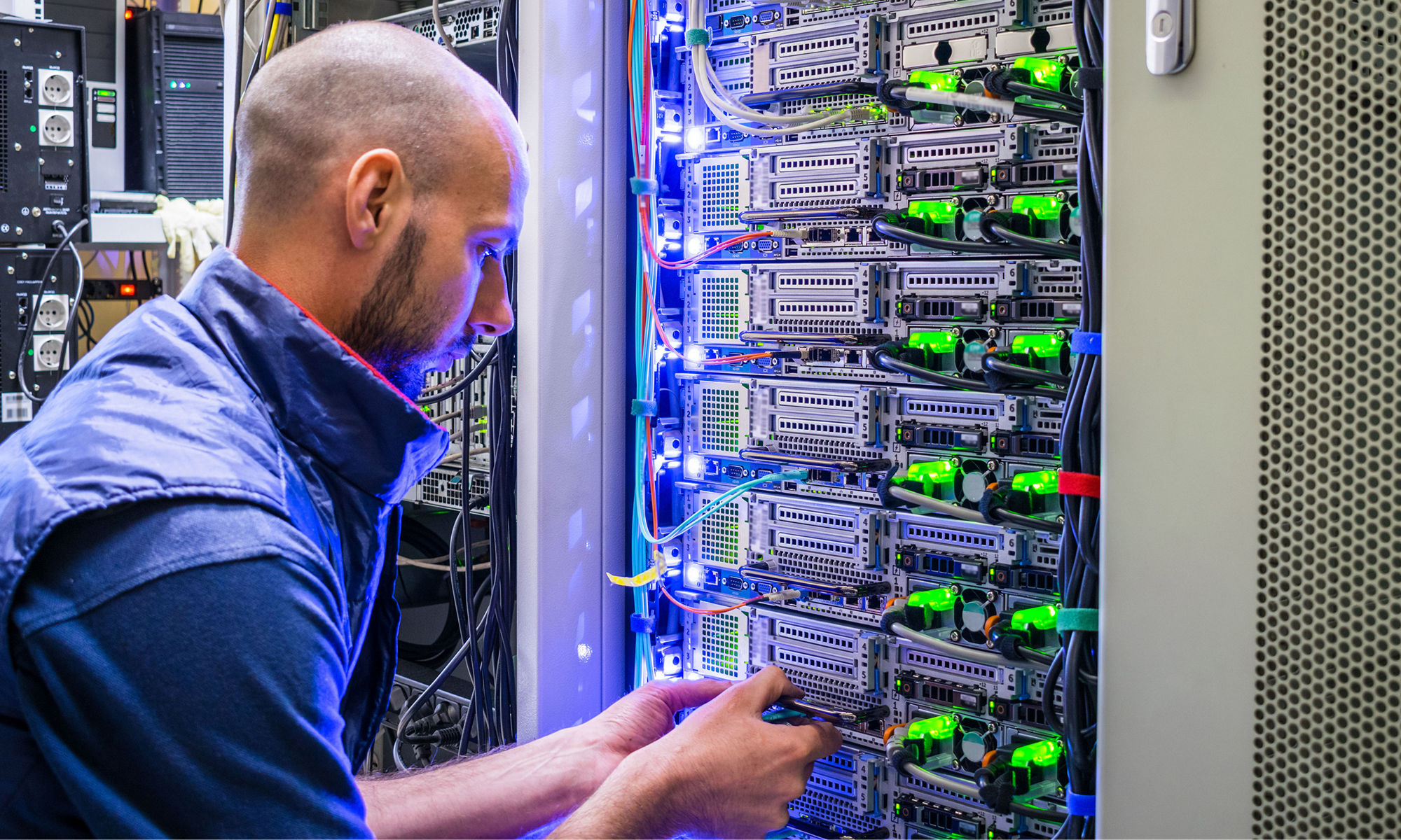  A man works with telecommunications. The technician switches the Internet cable of the powerful routers. A specialist connects the wires in the server room of the data center.