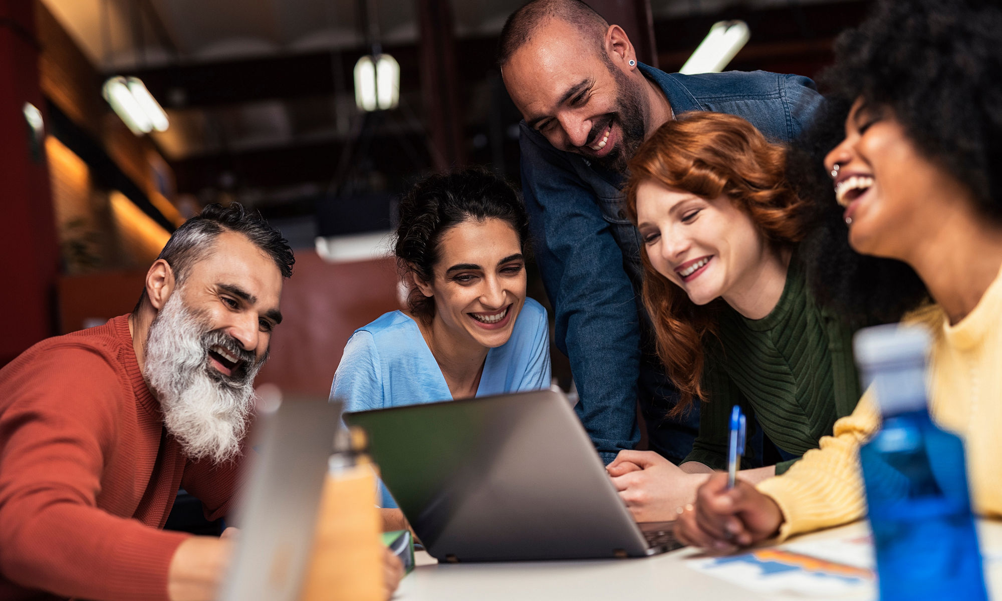 Group of five smiling co-workers sitting around a laptop