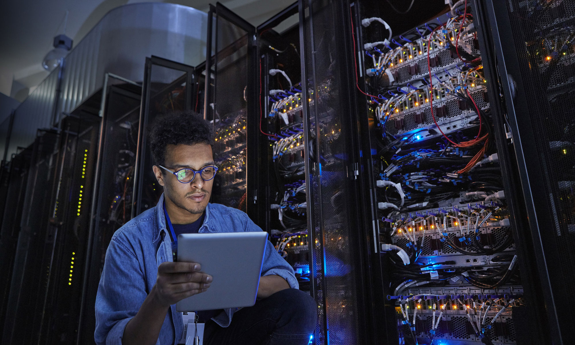 Focused male IT technician using digital tablet in dark server room