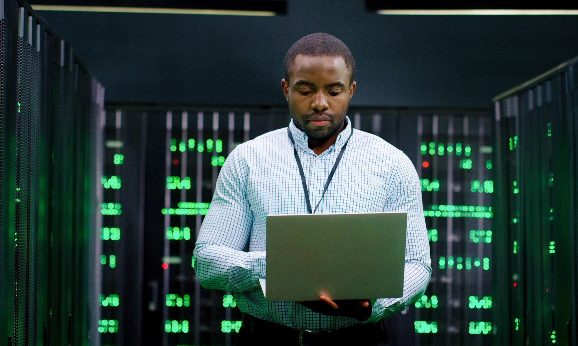 Male system administrator of big data center typing on laptop computer while working in server room. Programming digital operation. Man engineer working online in database center. Telecommunication.