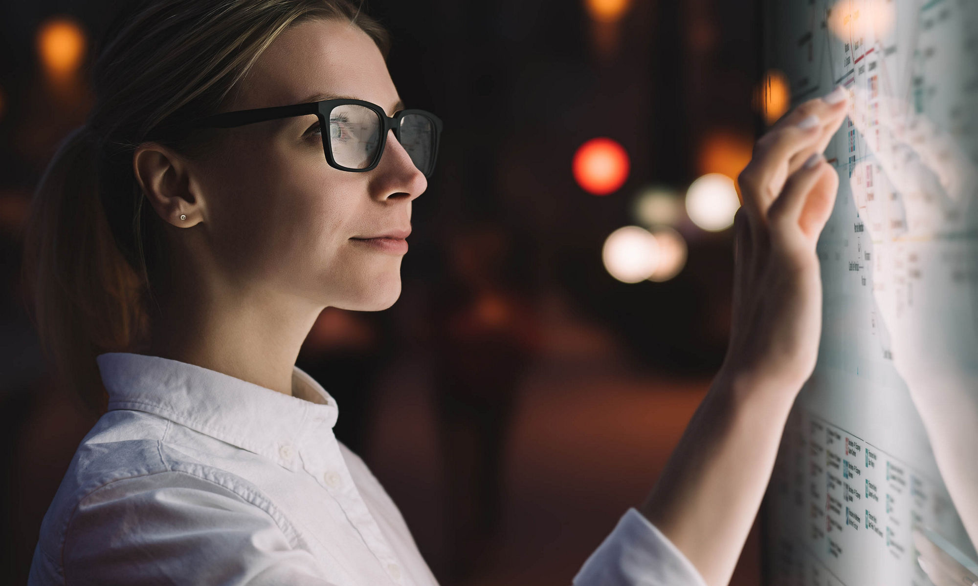 Digital monitor with public transport subway map. Female standing at big display with advanced innovative technology. Young woman touching with finger sensitive screen while selecting surface option