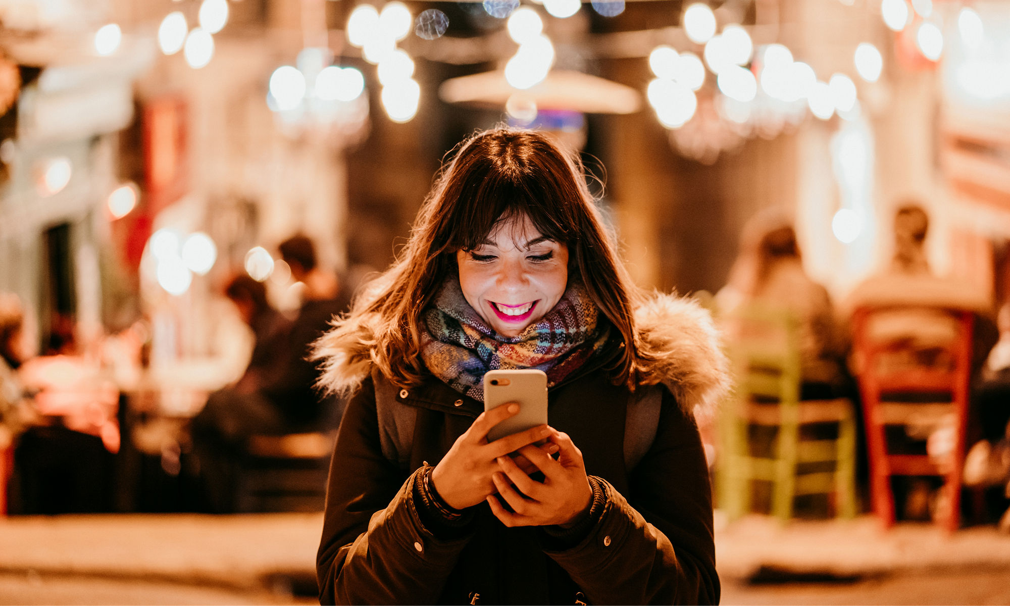 Young woman looking happily at her cell phone with a blurred social setting in the background