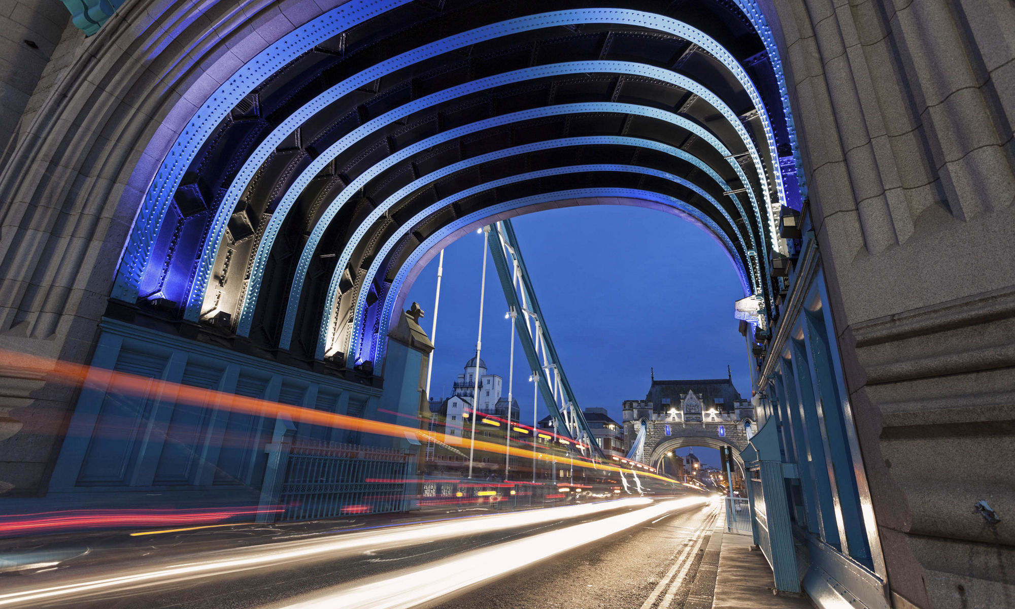 View coming out of a tunnel of blue lit night sky with bridge and city lights in the background