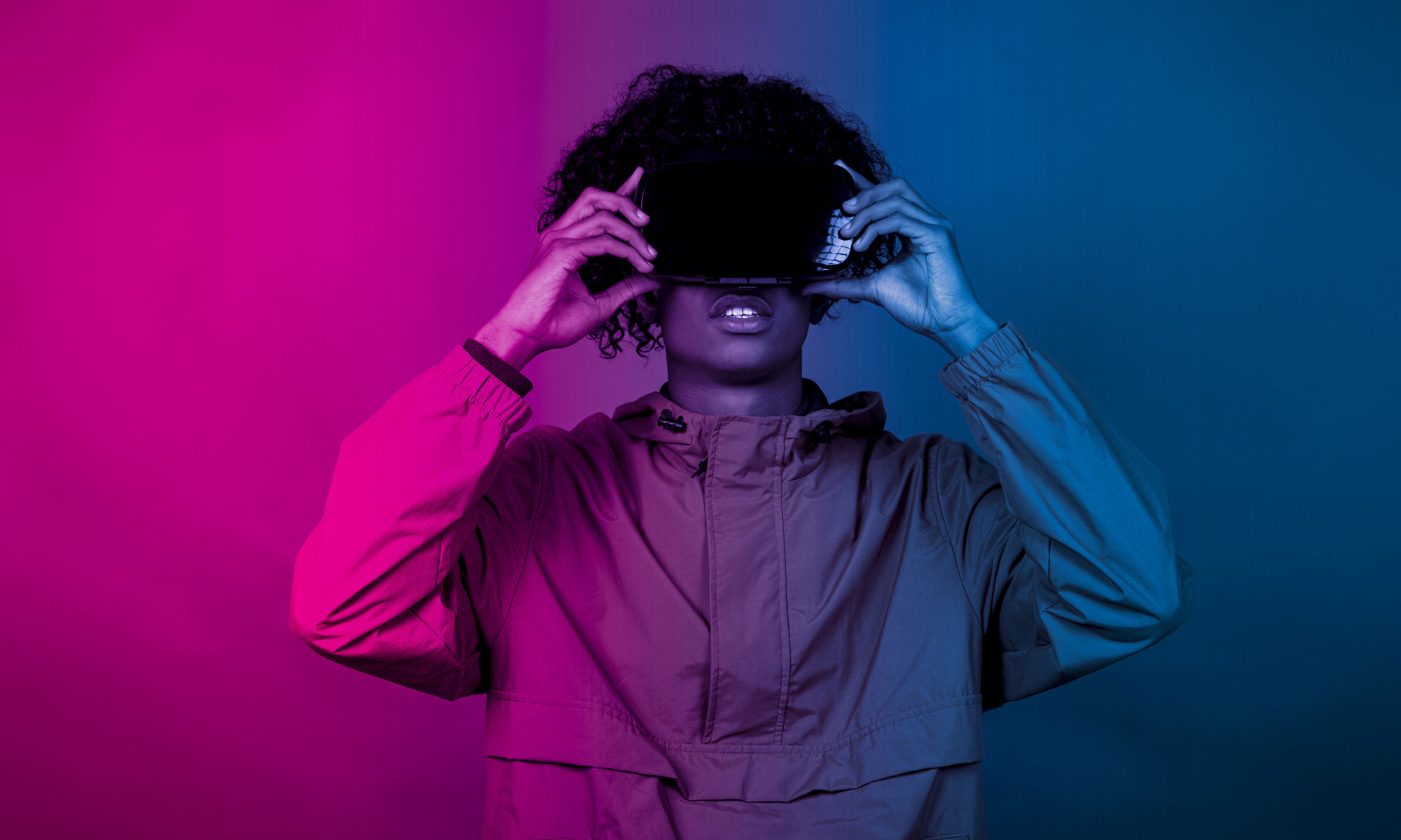 年輕的非裔男性帶著 VR 眼鏡站在藍色和紫色的燈光下