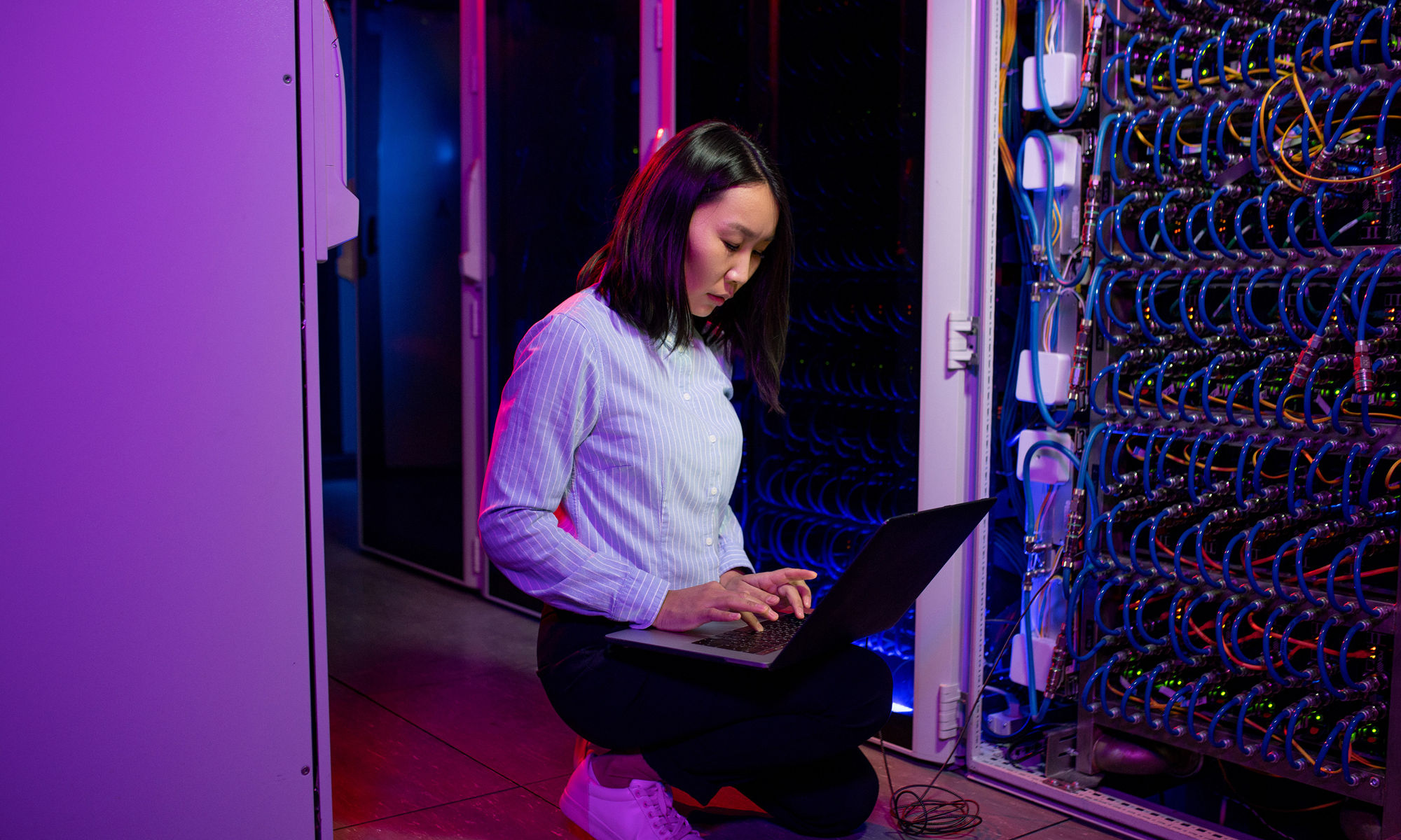 Kneeling woman working on a laptop in a server data center