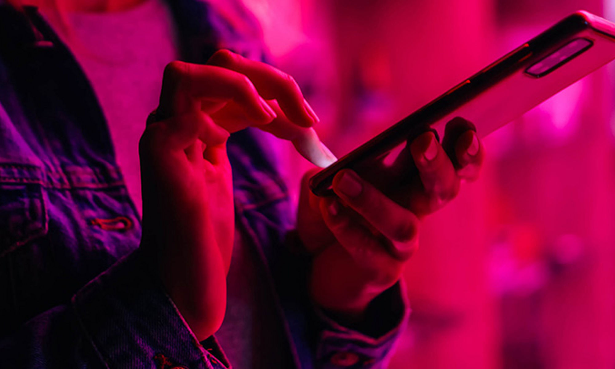 Close-up side view of a person tapping on a mobile device with purple to pink overlay