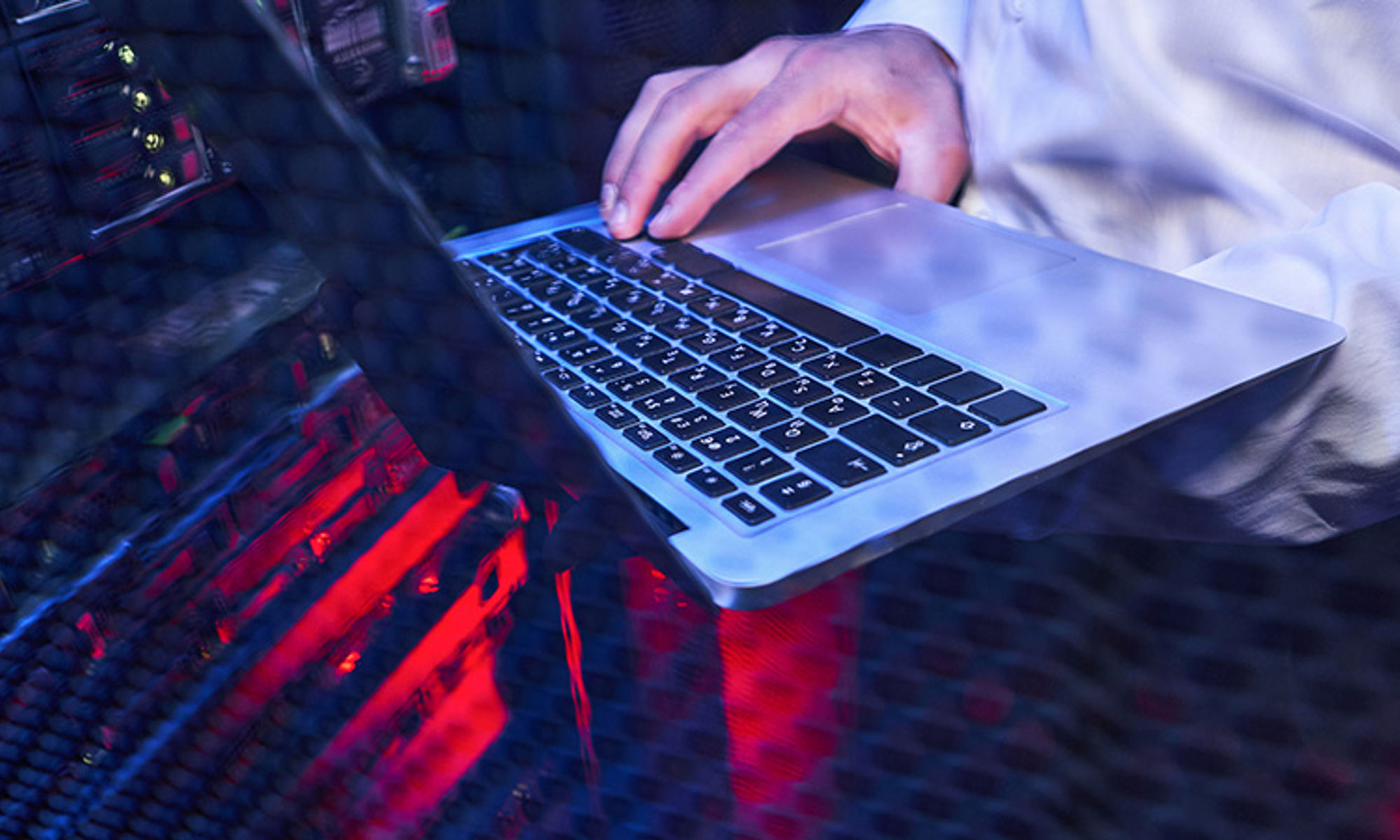 A laptop on a clear desk with red underlighting and a hand touching the keyboard.