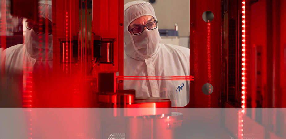 Person wearing a white clean room body suit and mask and looking into the room lit with red light