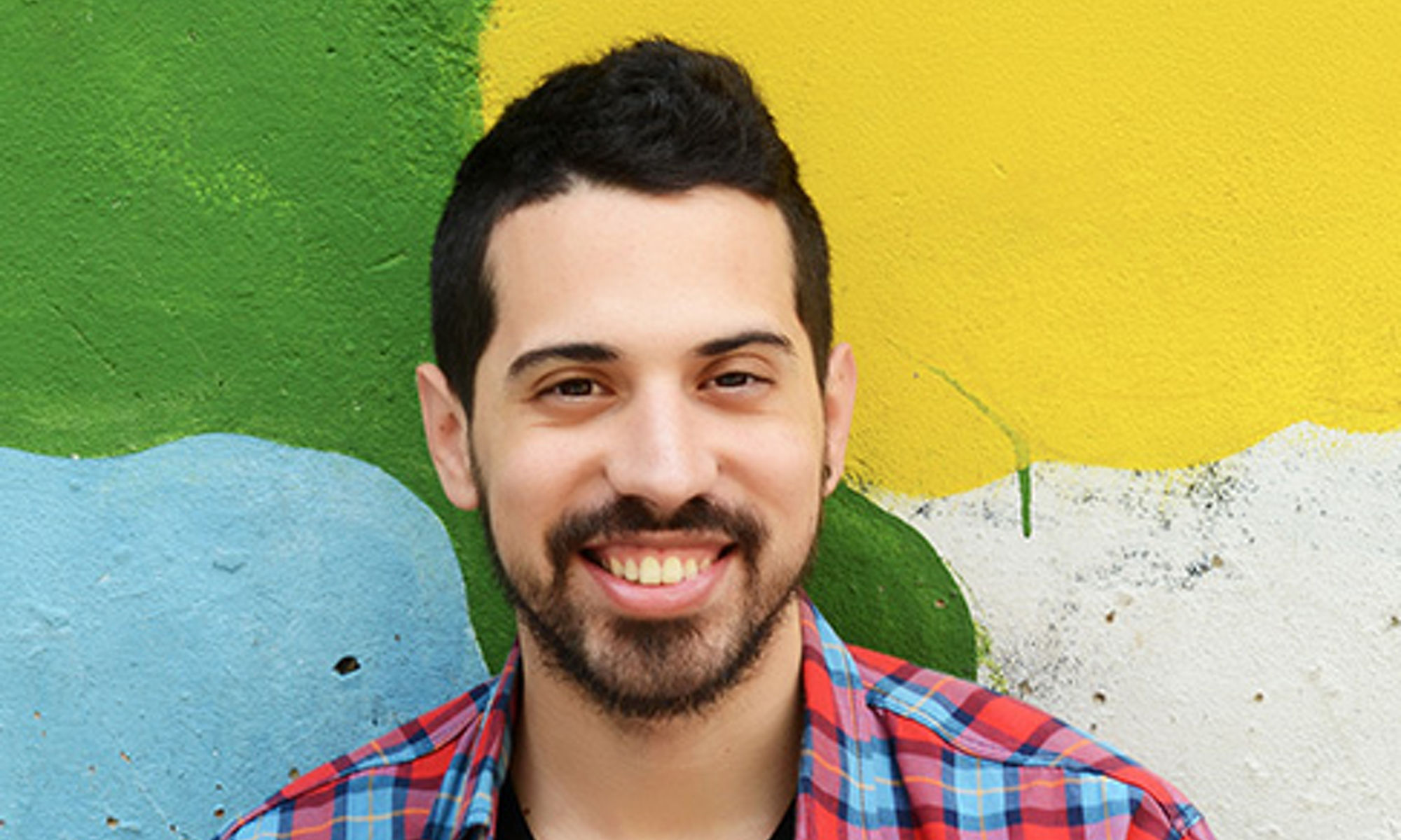 A man with a goatee smiling in front of a multi-color wall.