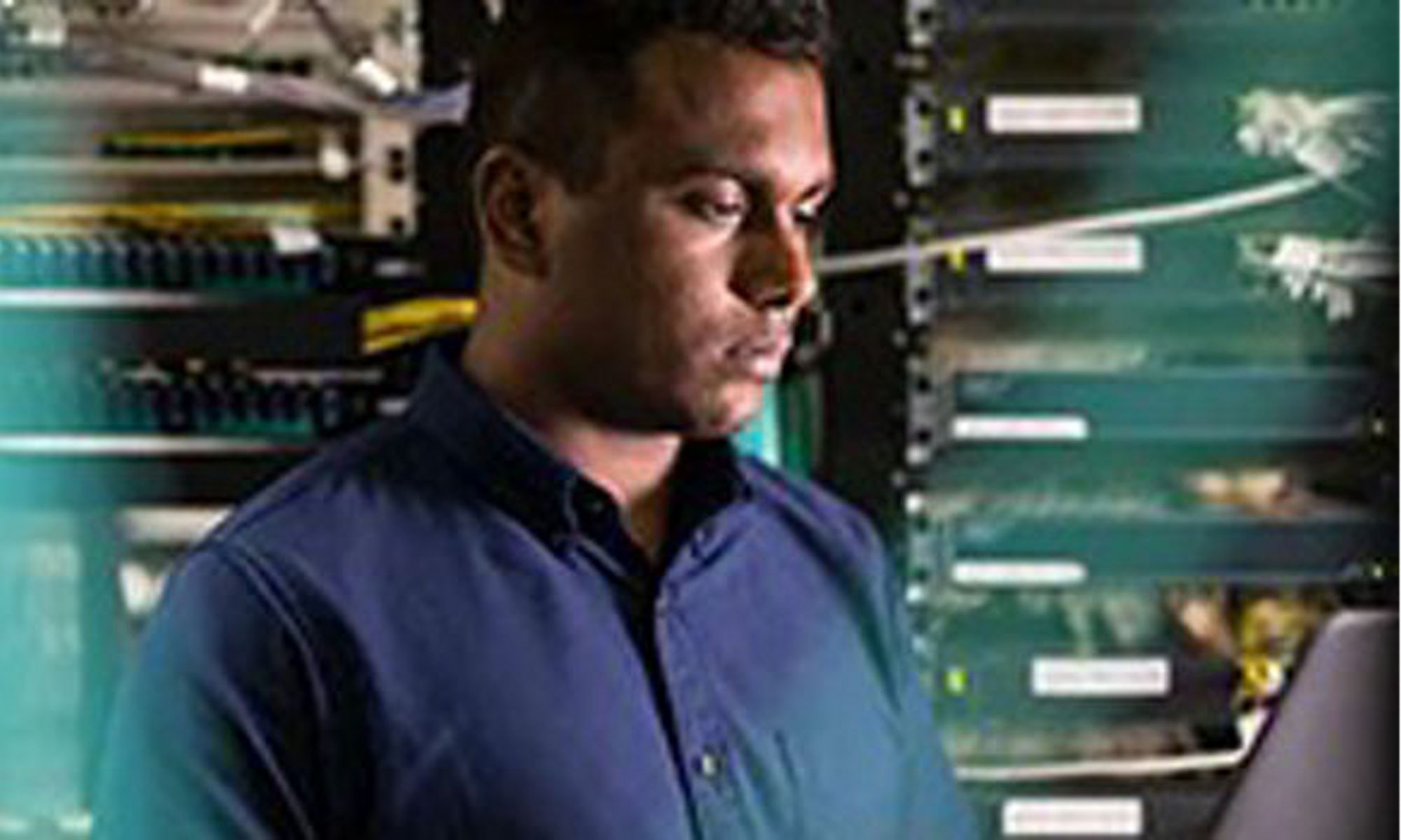 Man in a server room looking at a laptop