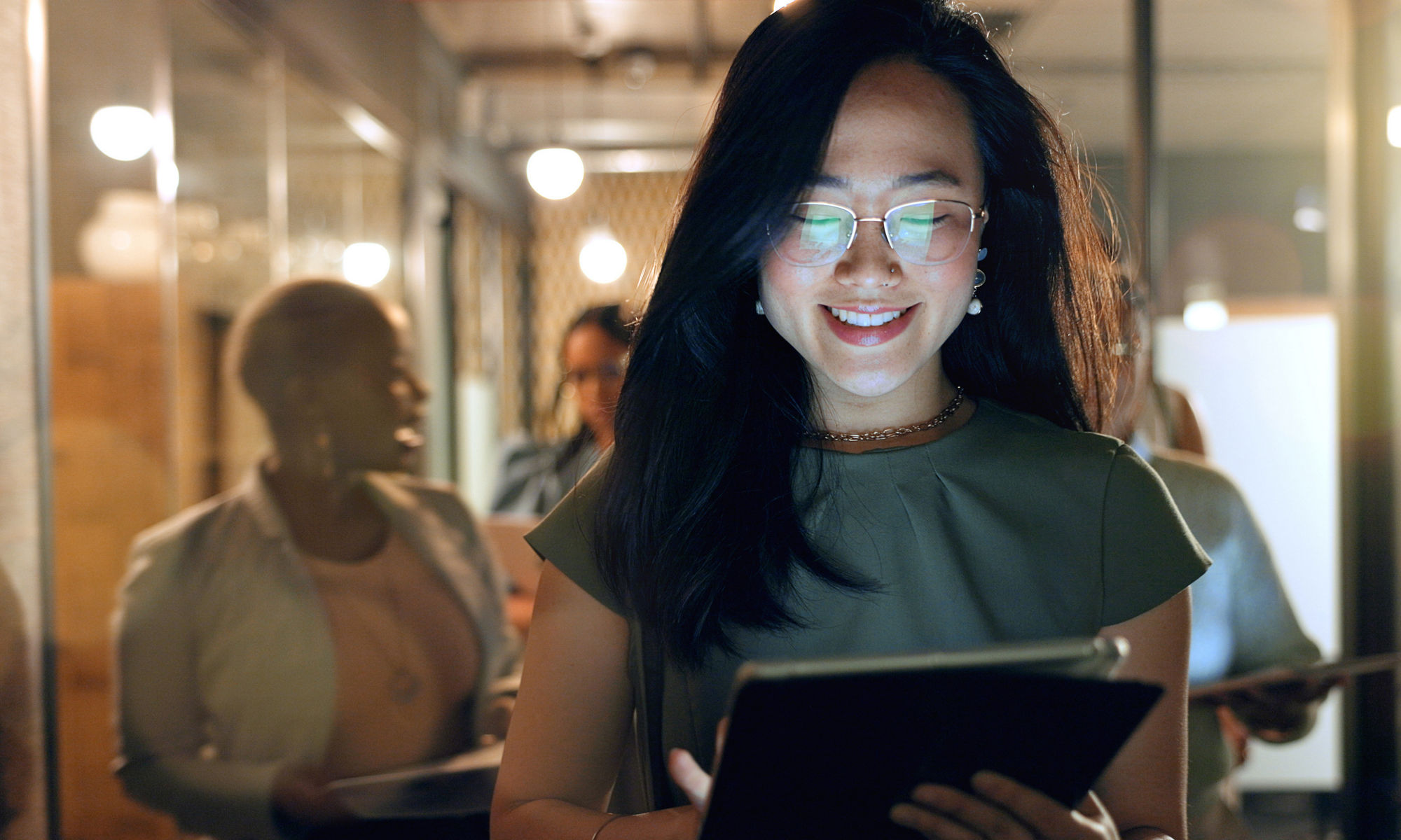 Smiling woman standing in office hallway reading a tablet