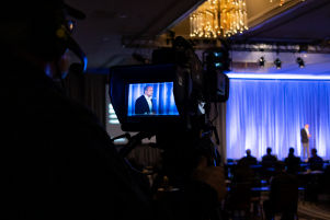 A screen showing the live telecast of the stage where a person is standing and addressing the audience