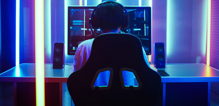 Gamer with headset sits facing his desktop in a neon lit room 