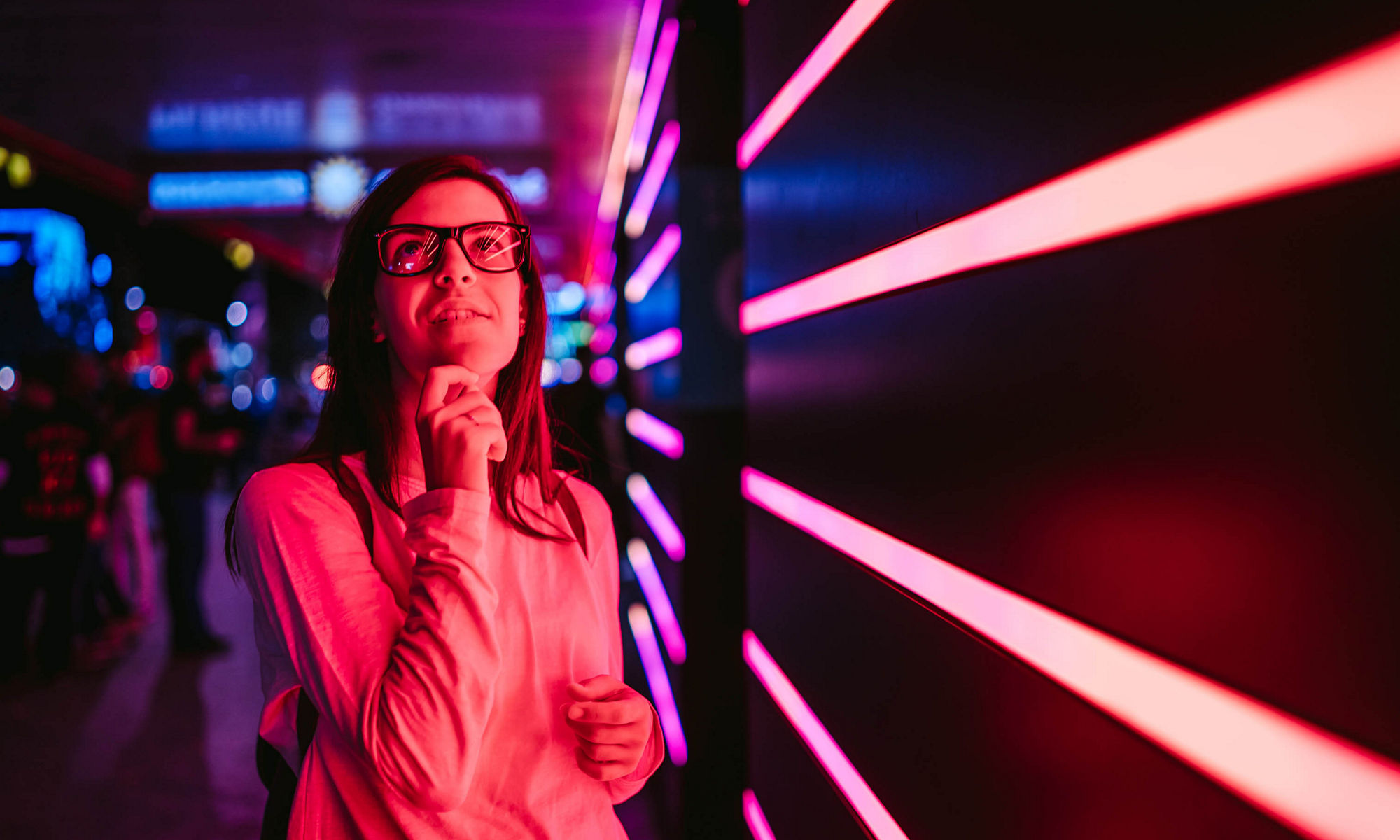 Young smiling woman with eyeglasses, standing in front of pink neon lights. Hamburg, Germany.