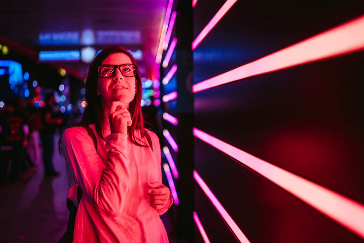 Young smiling woman with eyeglasses, standing in front of pink neon lights. Hamburg, Germany.