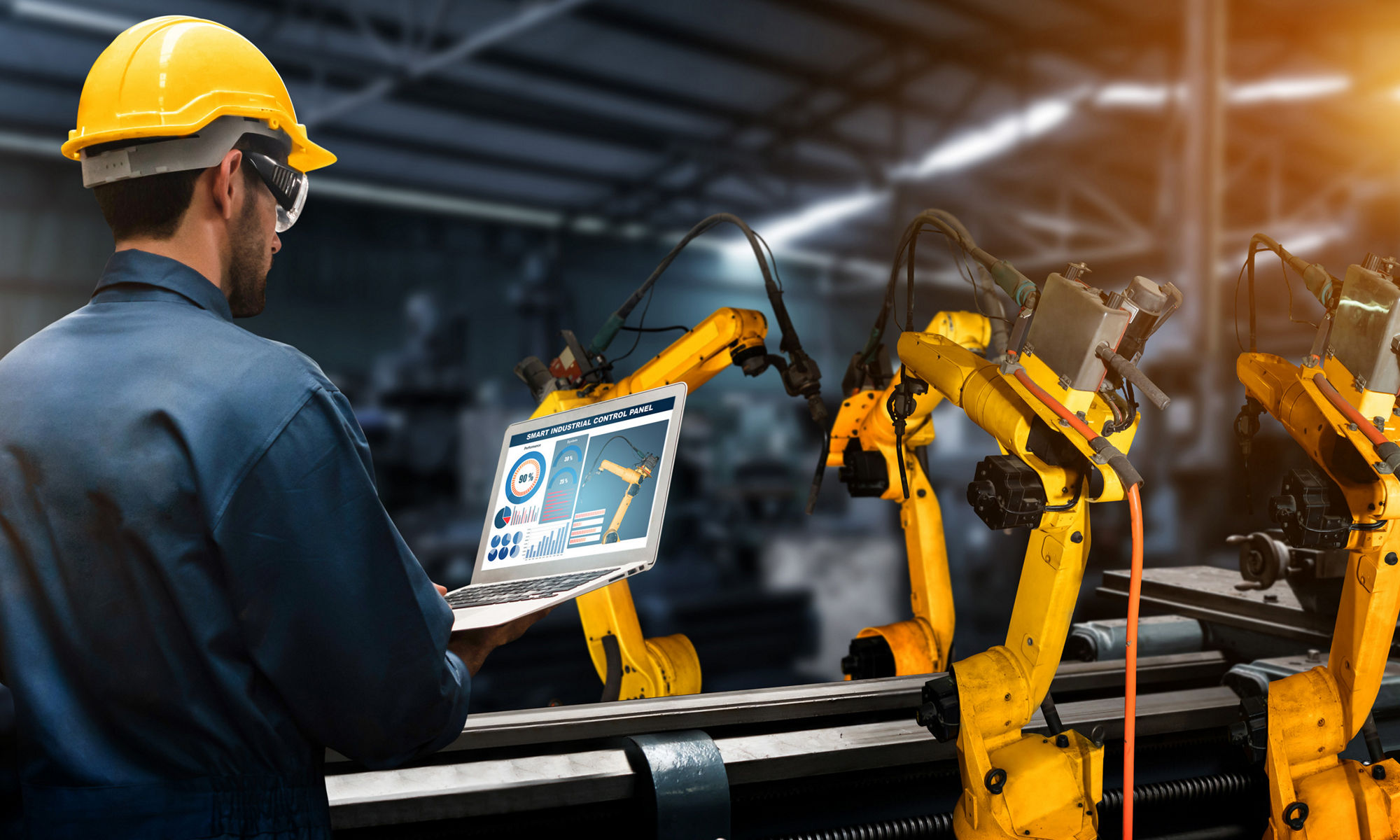 Multiple robot arms being programmed by worker in a hardhat