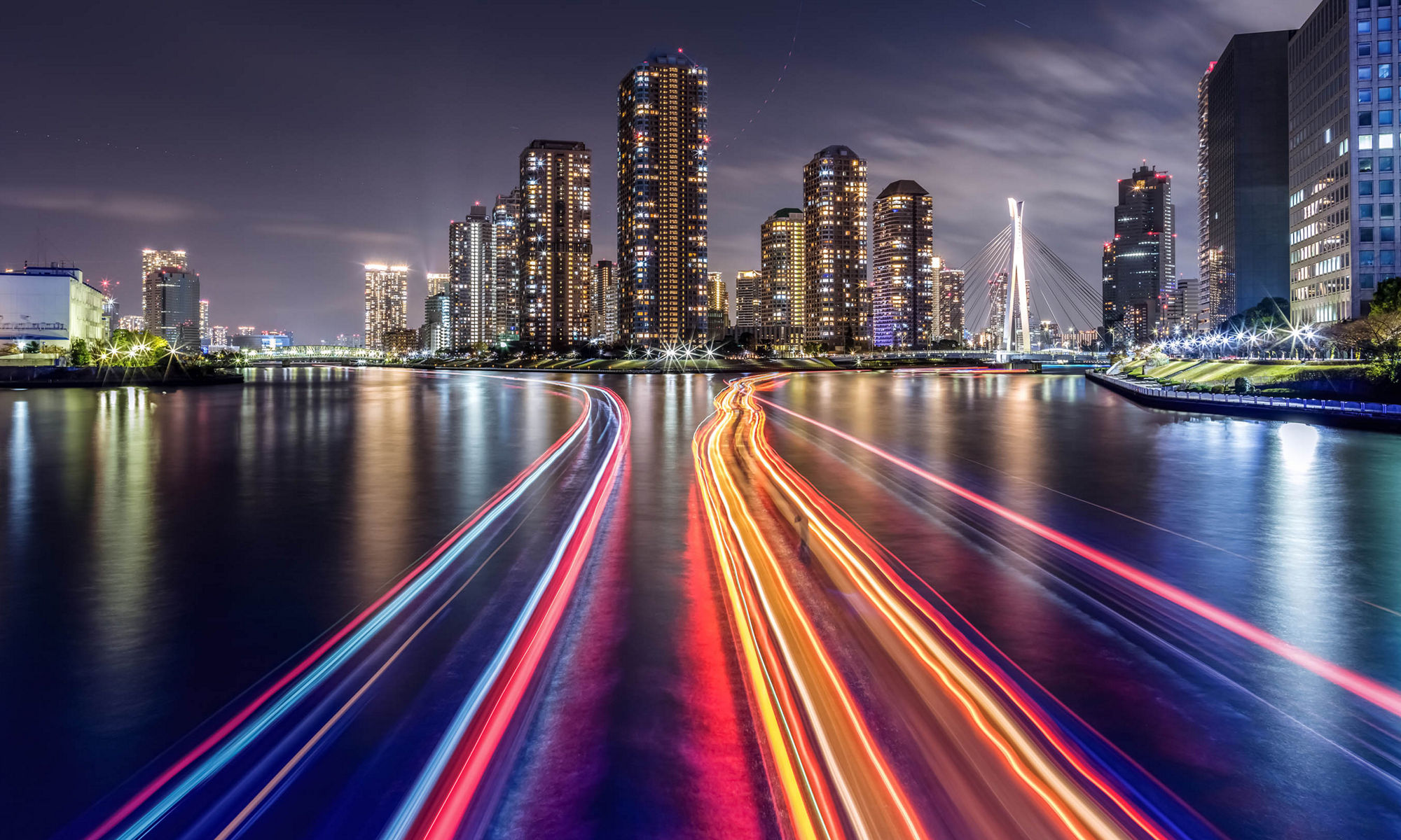 Tokyo skyline in Tsukishima aera, with high tall residential buildings illuminated over Sumida river with houseboat light trails in koto ward, Japan in the summer.Eitai bridge illumination reflection in the water and buildings light make a Romantic atmosphere.
