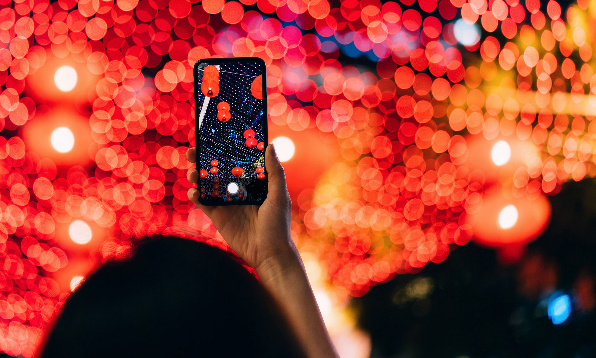 A view from above of someone holding their cell phone out over a sea of blurred bright lights in red and orange hues