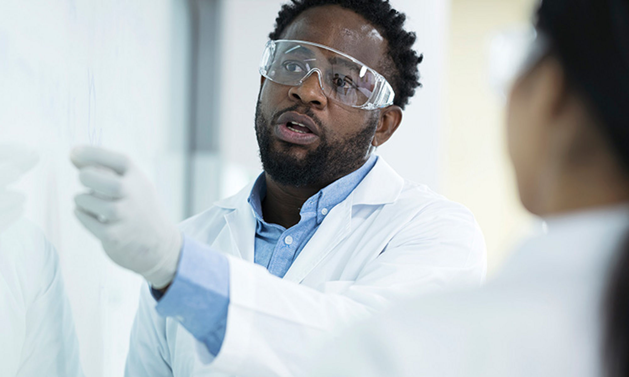 lab worker wearing gloves and goggles writing on white board