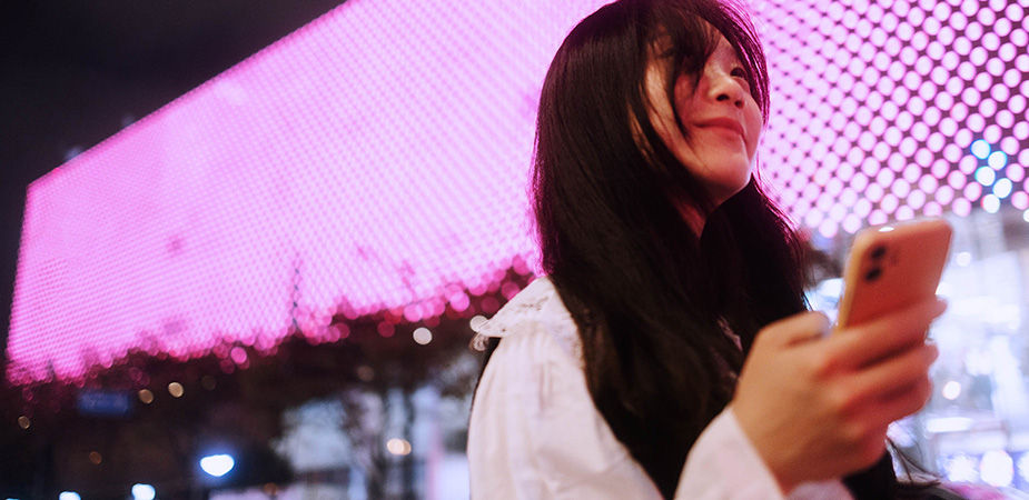 Woman using her phone at night, standing in front of a wall of LED lights