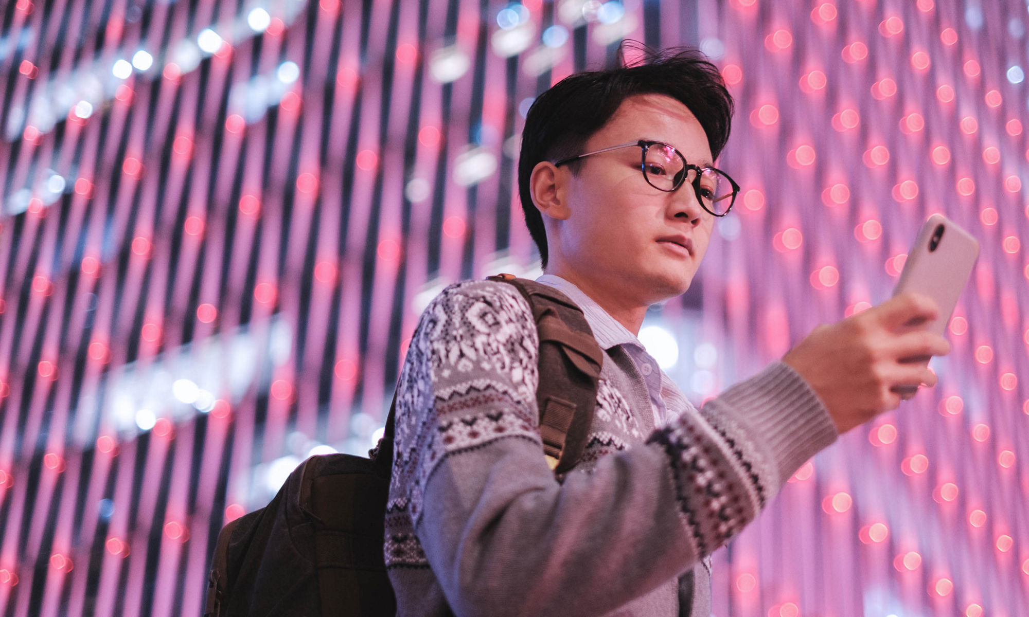 young man looking at smartphone standing in front of high-rise building