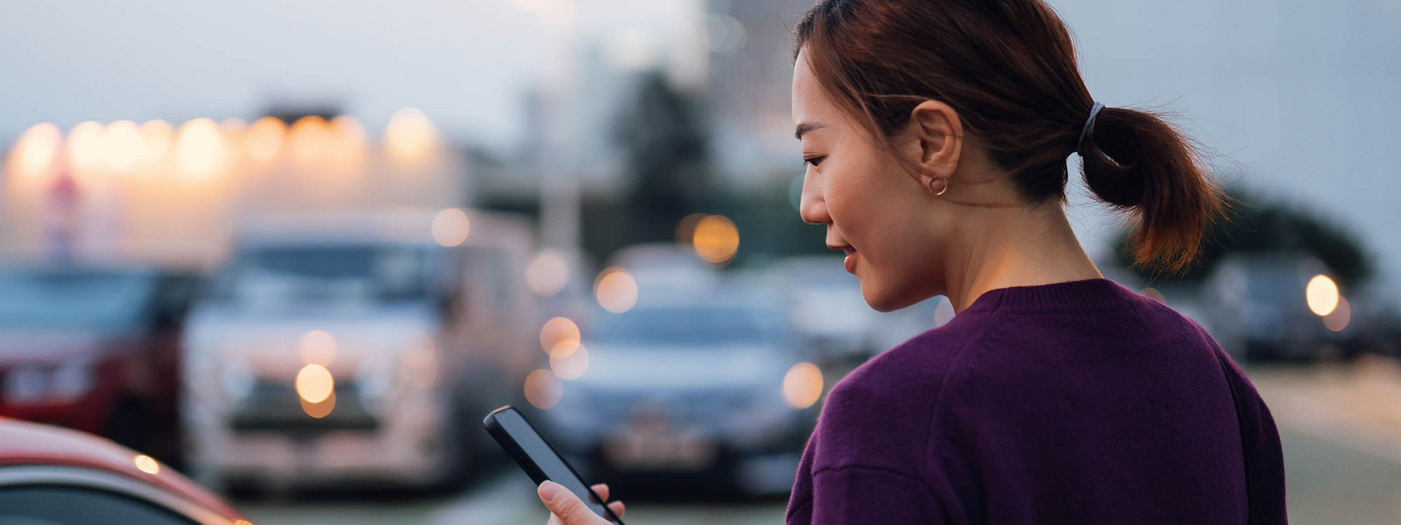 Young Asian businesswoman using smartphone while walking to her car, commuting in the city, with urban cityscape in background. Business on the go concept