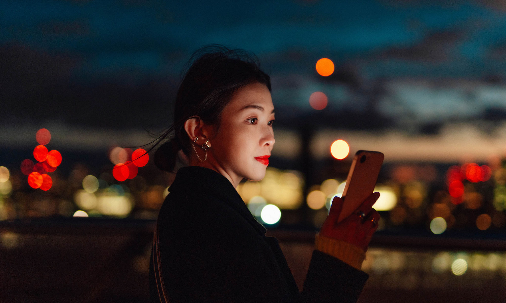 Woman looking at her phone, at night.