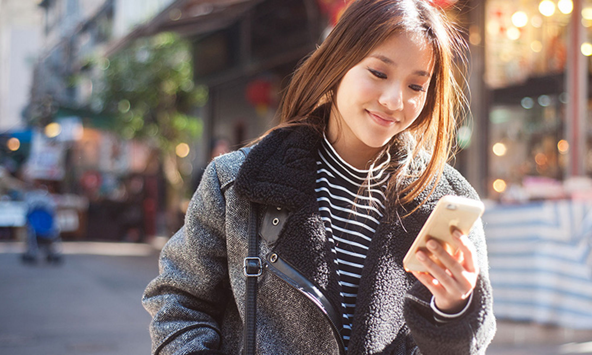 外でスマートフォンの画面を見ている女性