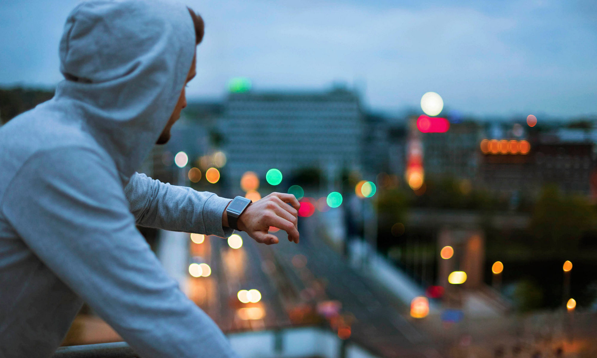 A man with his arm tilted to display the face of a smartwatch, overlooking a city.