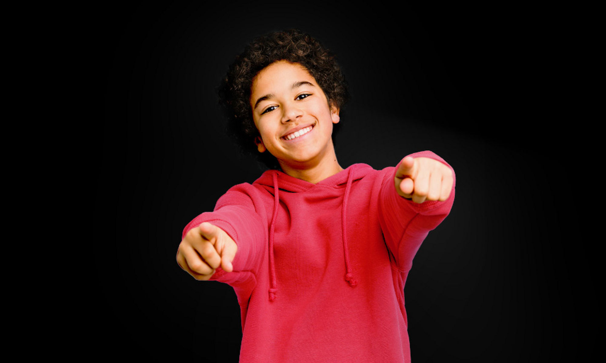 Smiling young person in a red hoodie pointing to camera