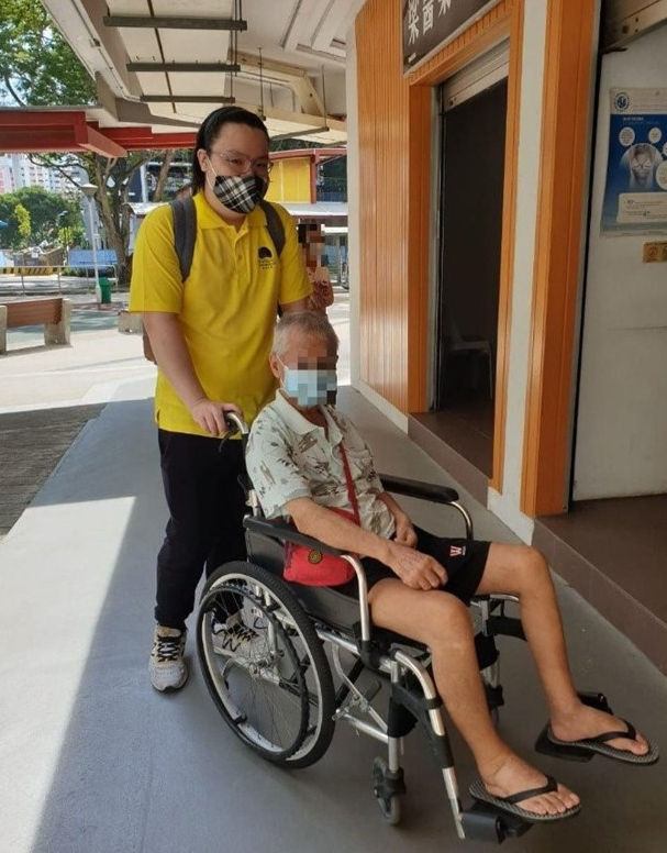 Jordon Ong volunteering with Seniors Befriending and pushing a man in a wheelchair