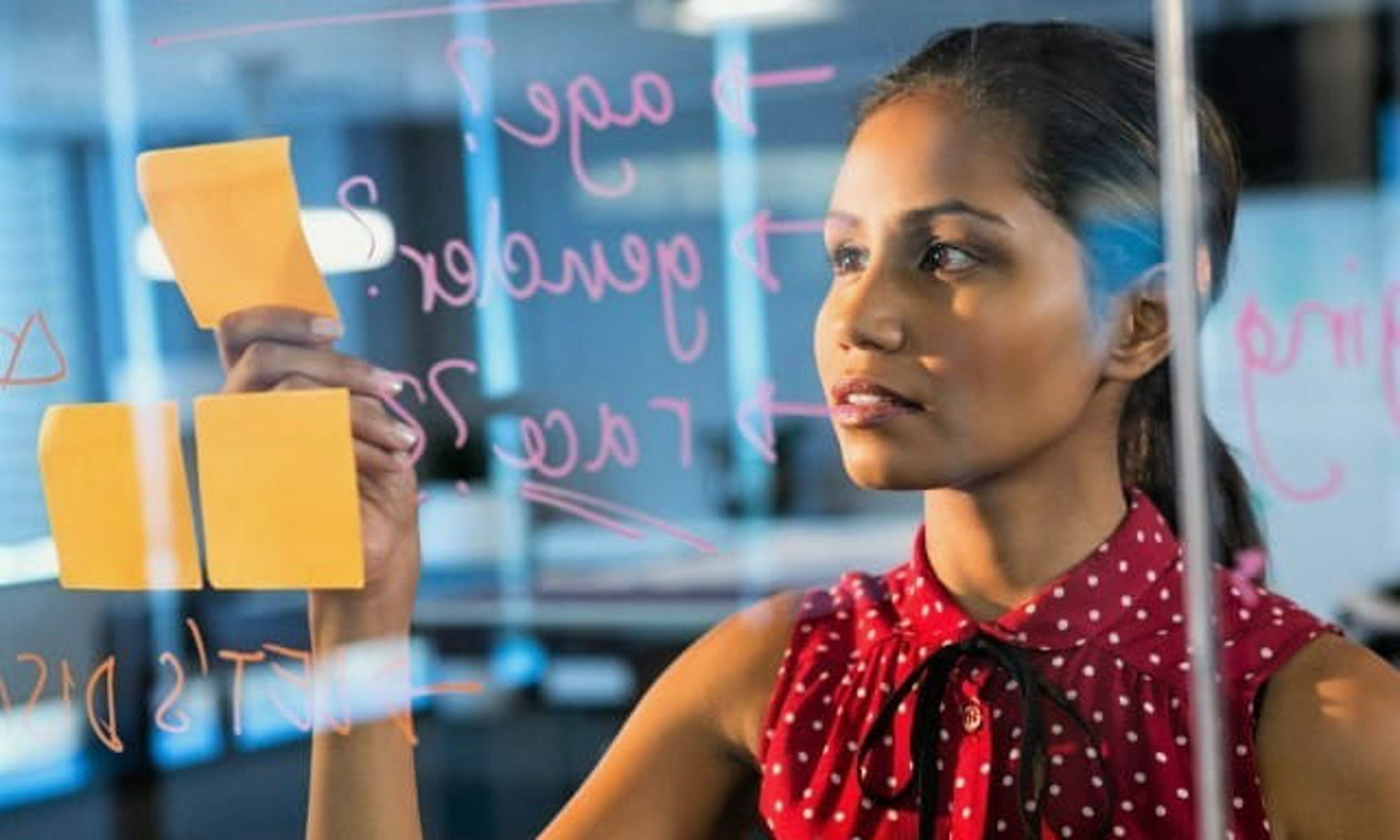 A woman writing on a glass wall and post-it notes.