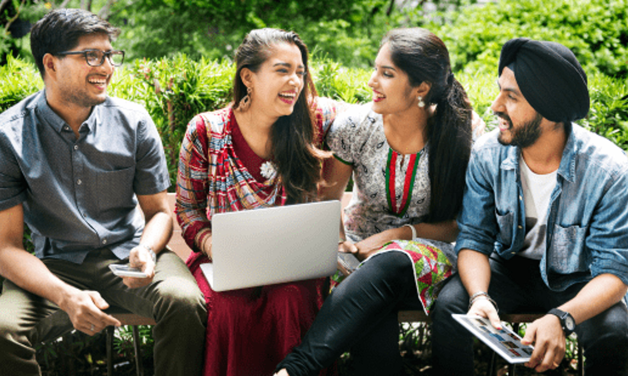 Two male and two female students talking outside holding laptop