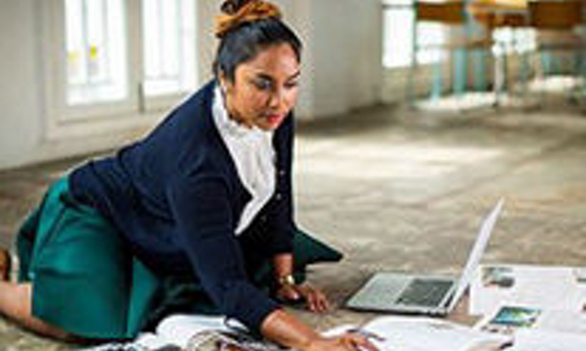 A woman sitting on the floor looking over paperwork and working on a laptop