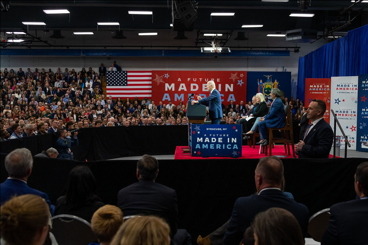 Room full of audience and press listening to president Joe Biden on stage