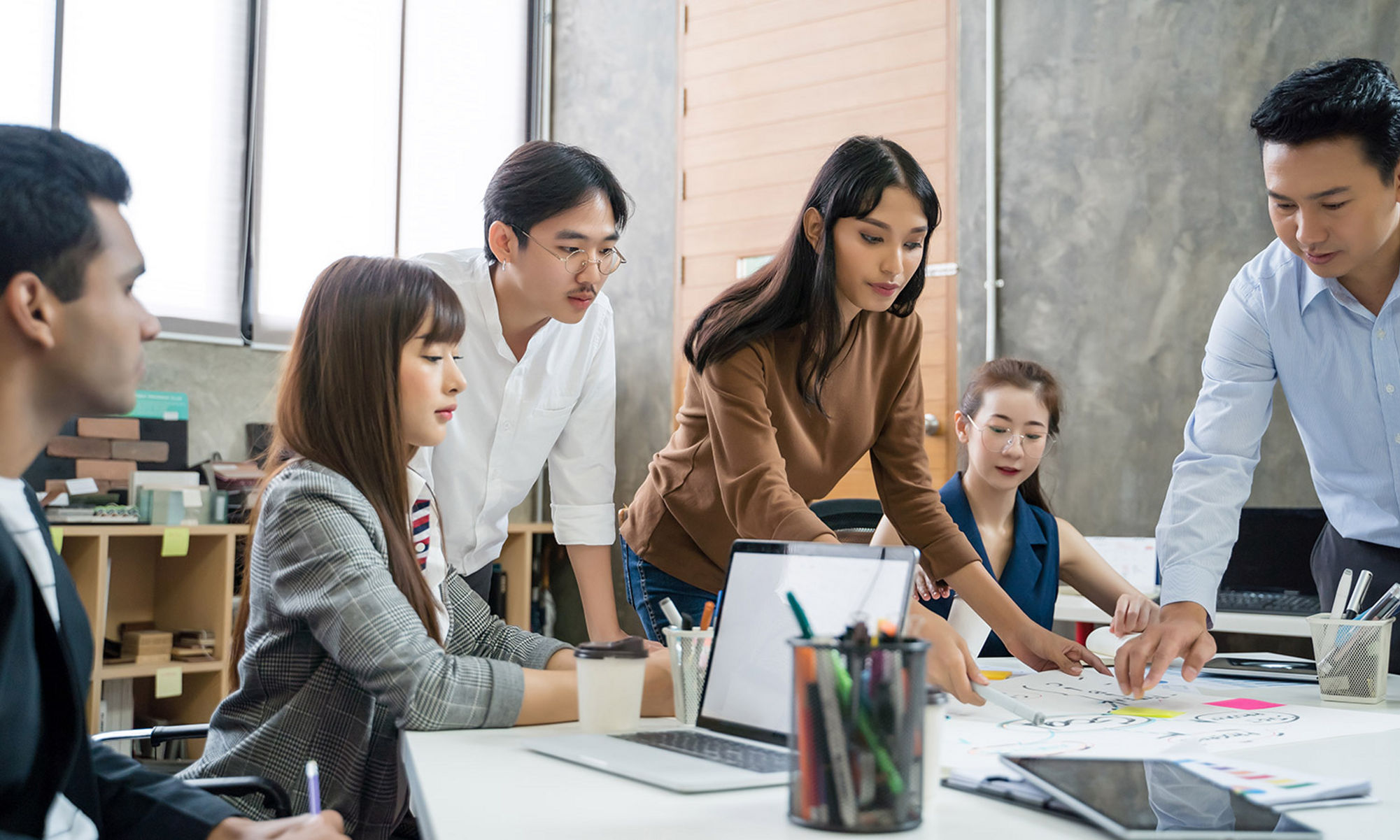 Group of students sitting at a table smiling around a laptop computer