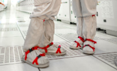 Two persons wearing a white lab coats head to toe, one holding a tablet in hand