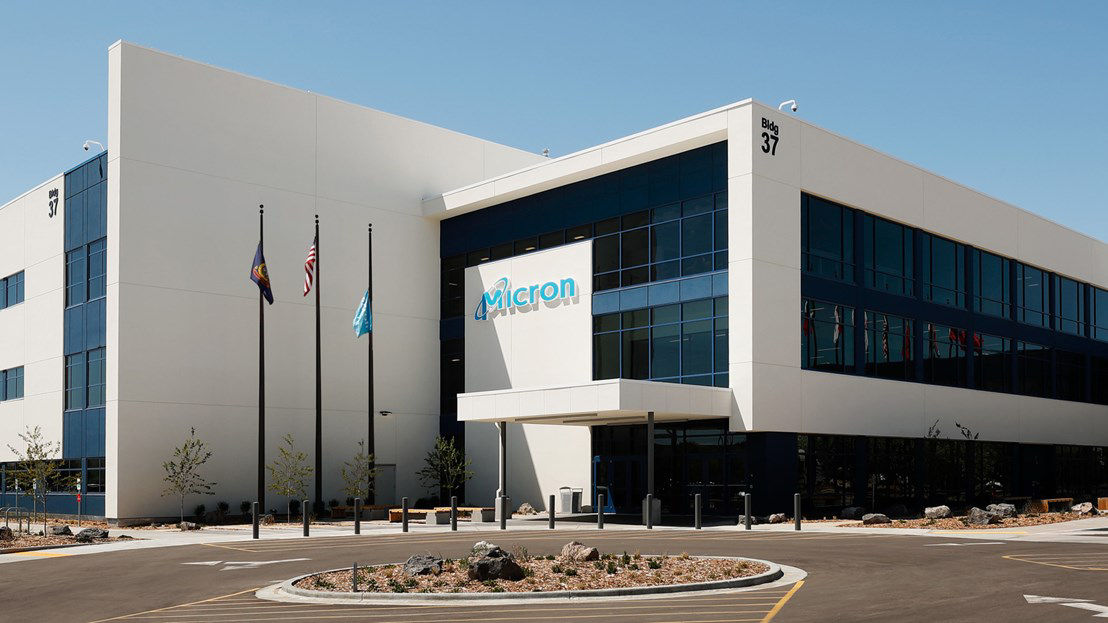 A building with 3 flag poles in front of it and micron written on the building