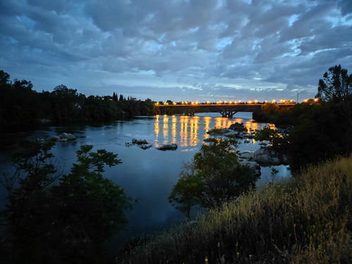 a river with a lit bridge in th background at dusk