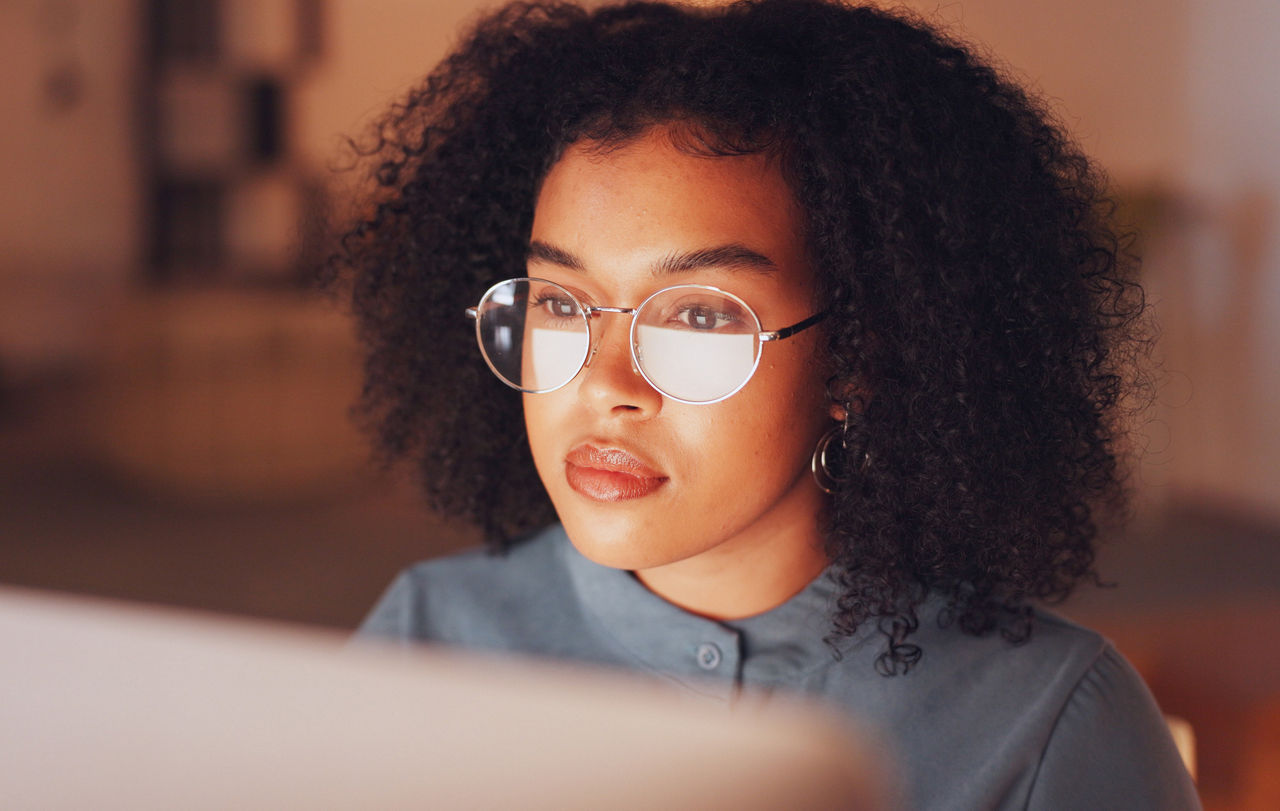 Woman of color reading a laptop in a dimmed room