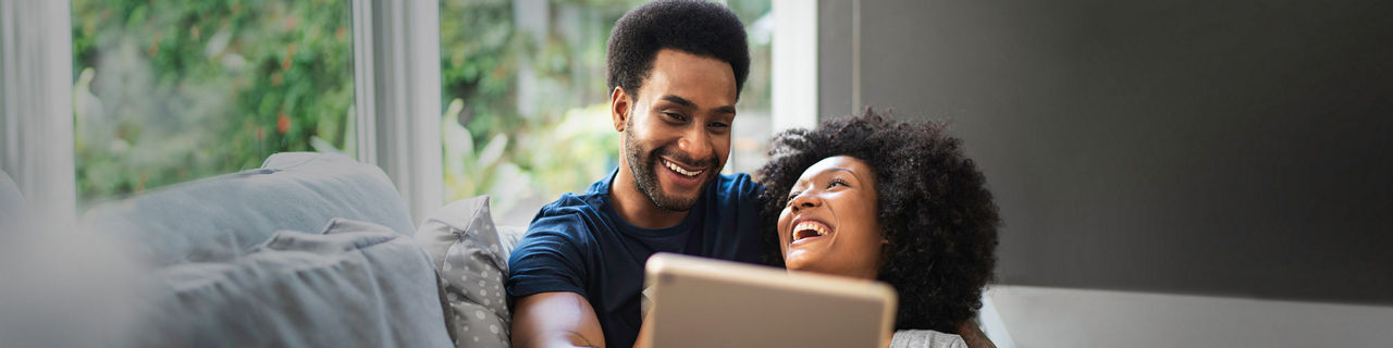 man holding his wife on a couch while using a laptop