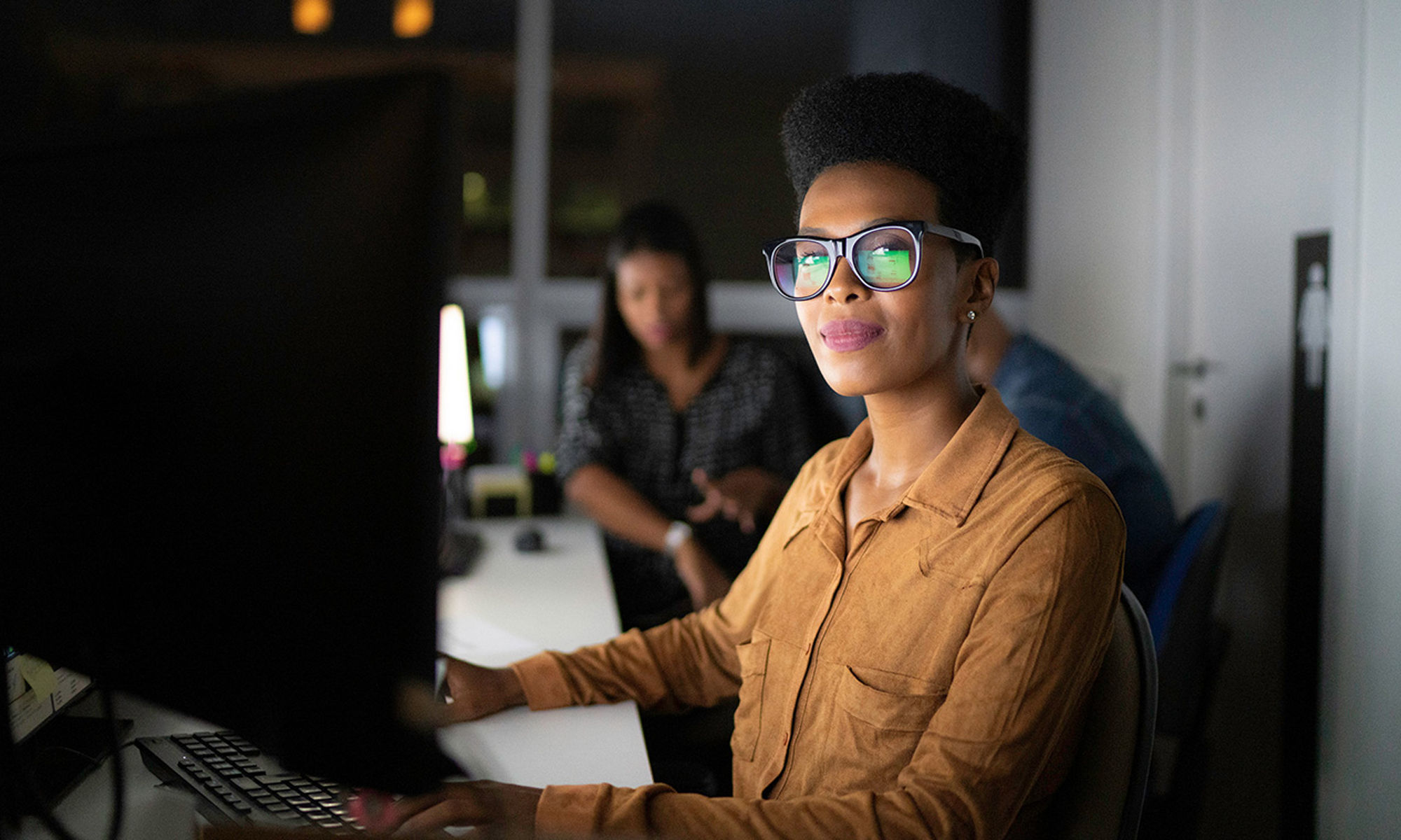 暗いオフィスの中でコンピューターで作業する女性