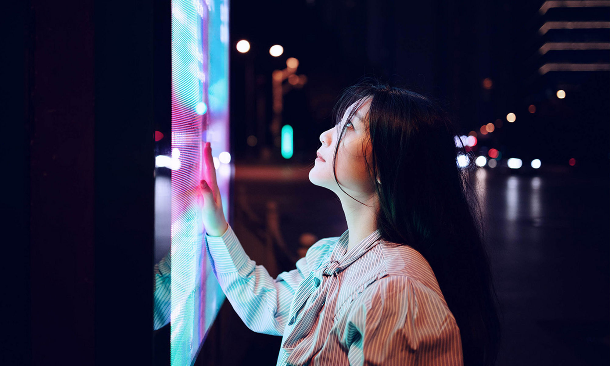 Woman interacting with a public touch screen, at night.