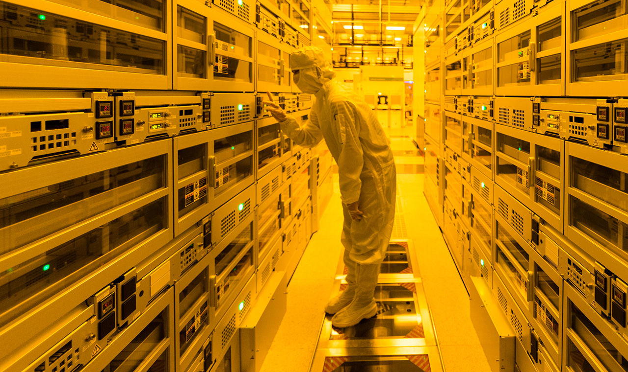 Workers in a fabrication clean room suit looking into a work area