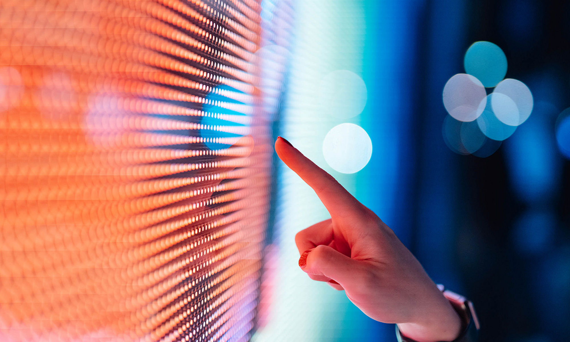 A hand, at night, about to touch an outdoor LED screen